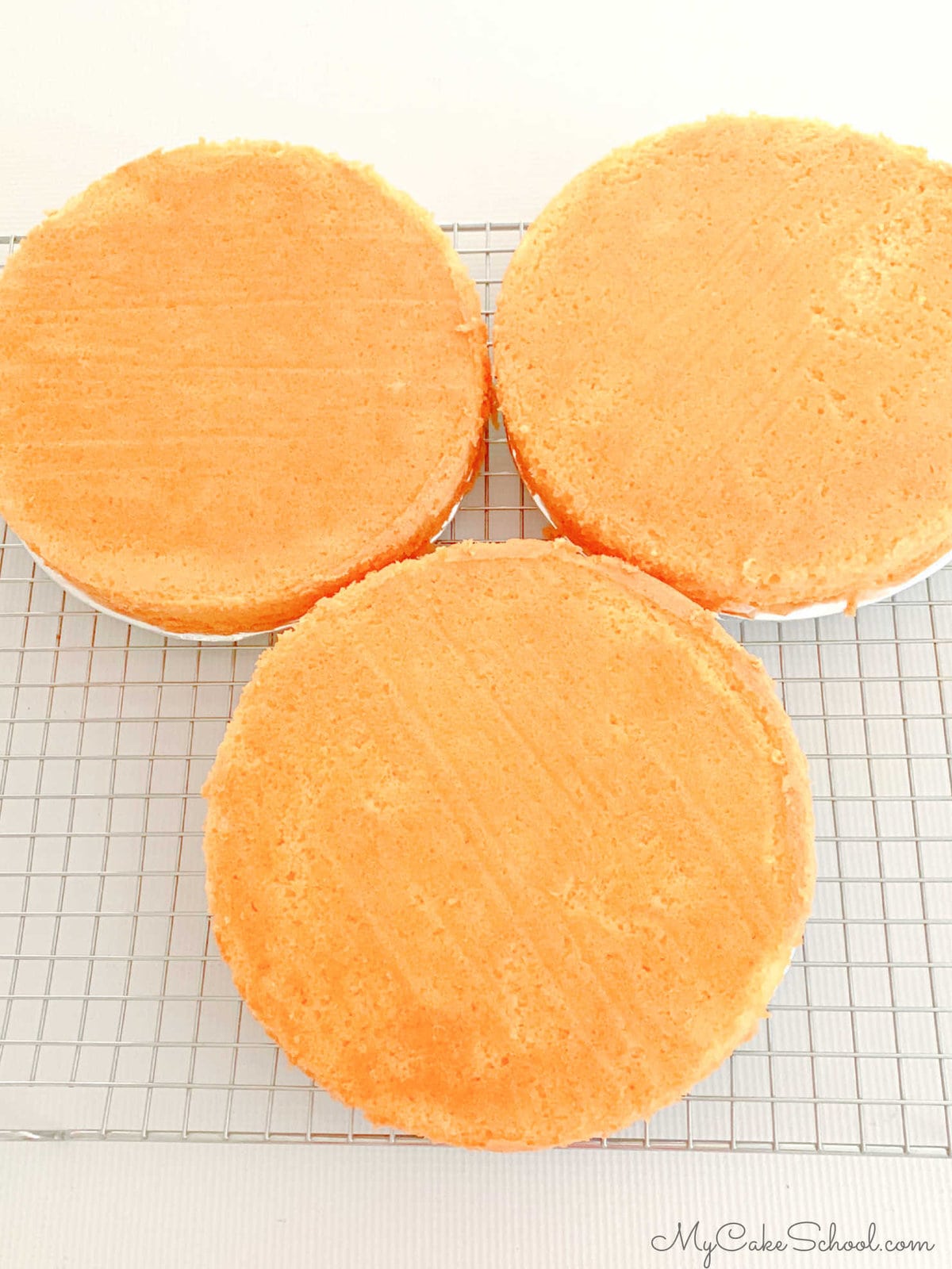 Three freshly baked orange cake layers on a wire rack.