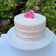 Semi-naked cake on a white cake pedestal, topped with fresh pink roses