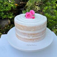 Semi-naked cake on a white cake pedestal, topped with fresh pink roses