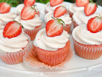 Frosted strawberry cupcakes on a platter, topped with strawberry halves.