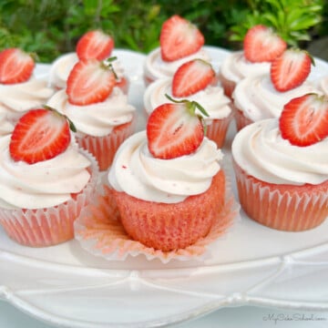 Frosted strawberry cupcakes on a platter, topped with strawberry halves.
