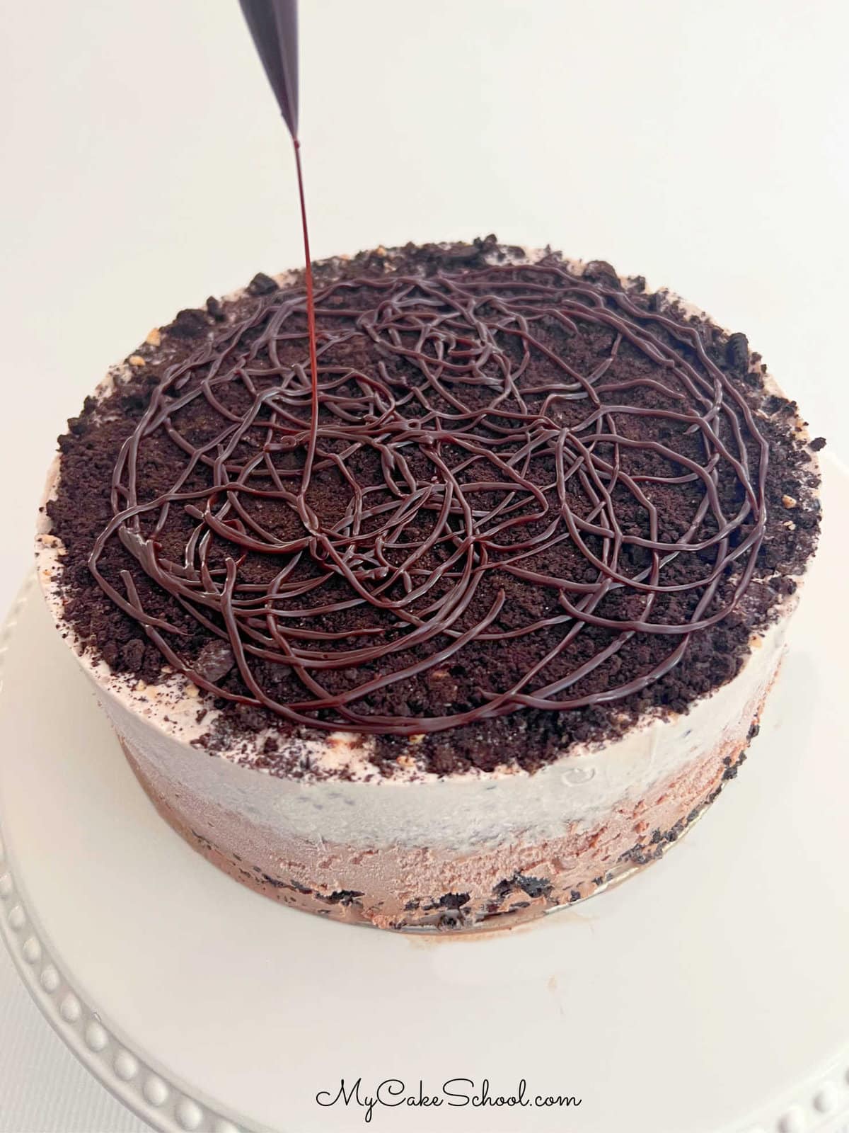 Drizzling top of Oreo Ice Cream Cake with hot fudge