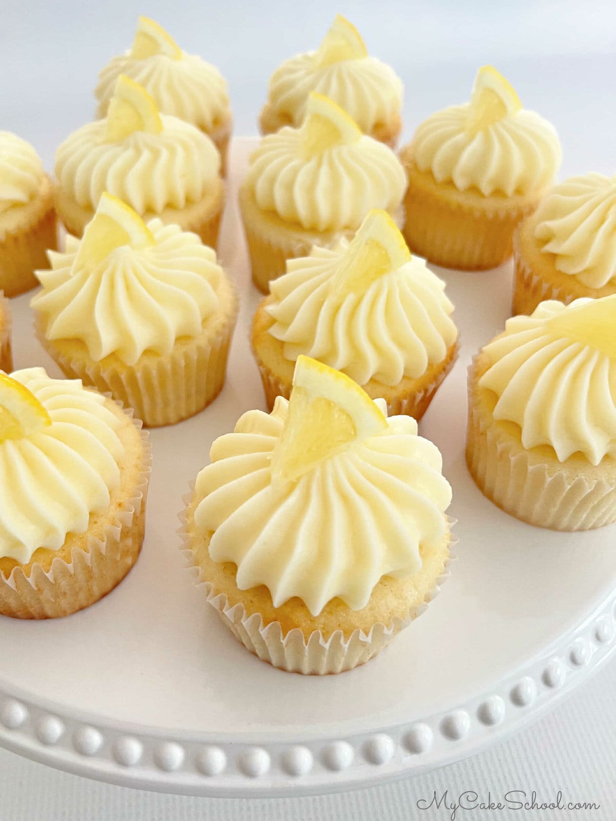 Lemon Cupcakes on white cake pedestal, topped with small slices of fresh lemon