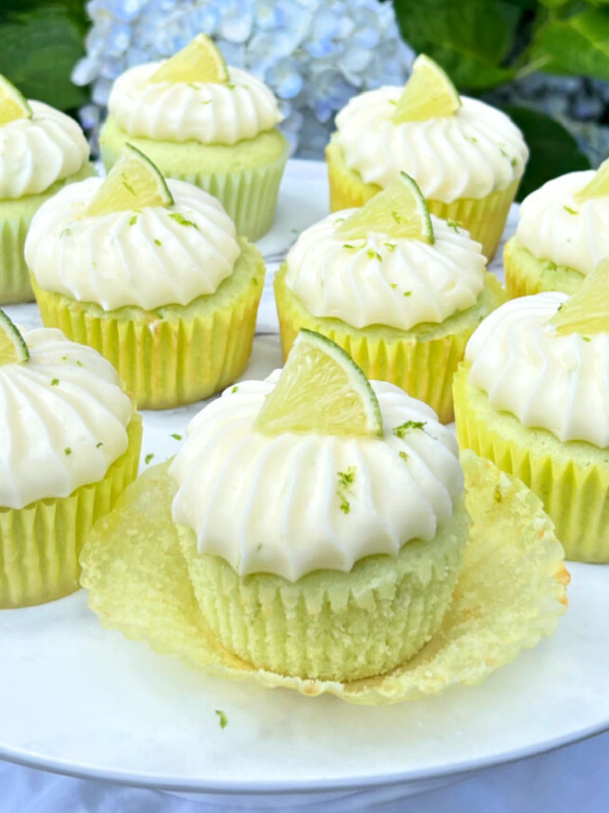Margarita Cupcakes topped with tequila lime frosting and lime wedges, on a white pedestal.