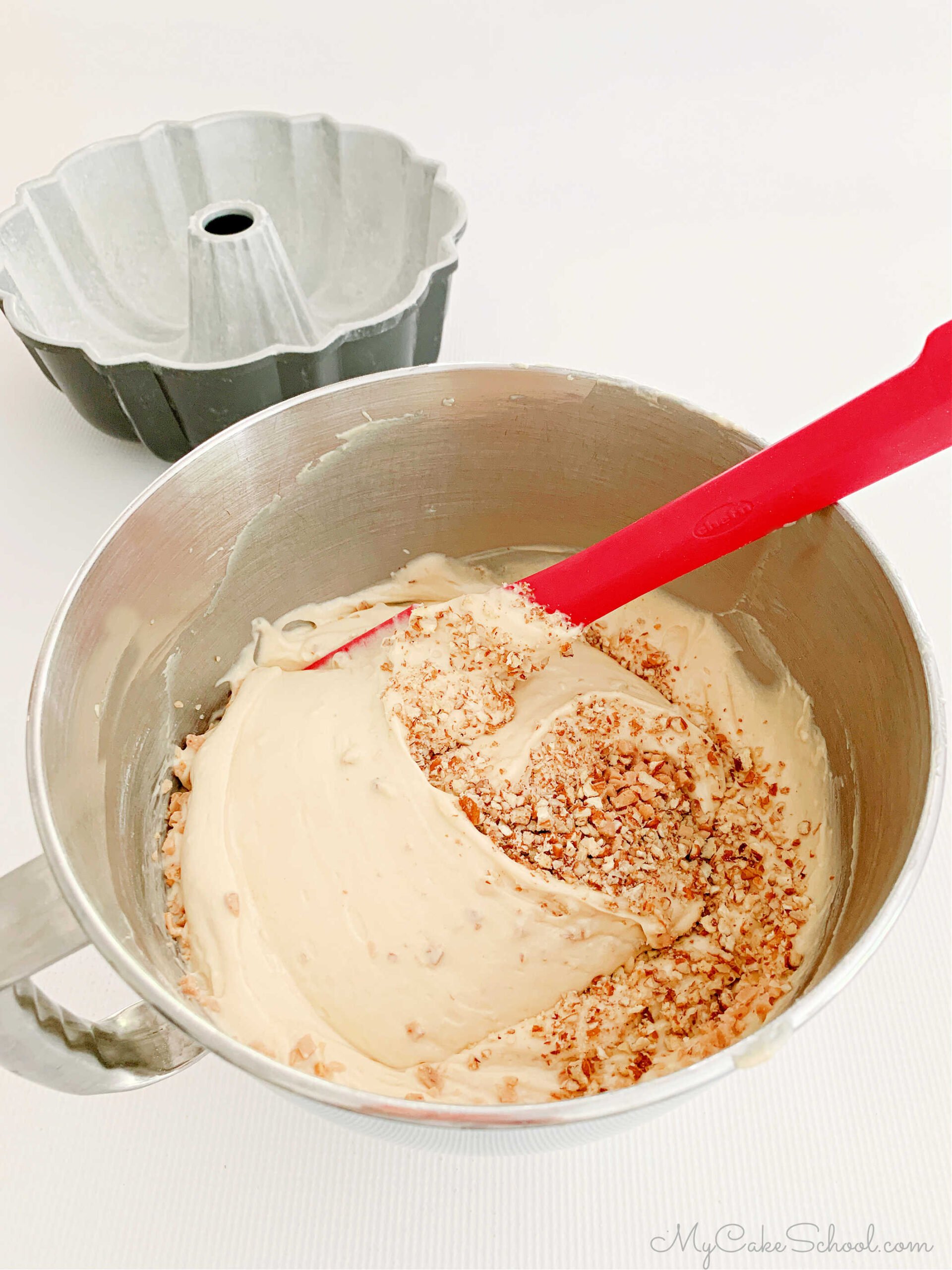 Folding toffee bits and pecans into bowl of cake batter with a rubber spatula