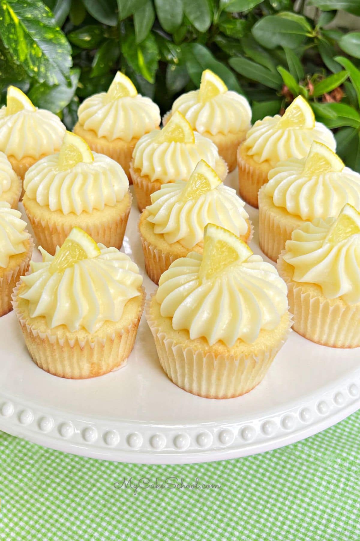 Lemon cupcakes frosted with lemon cream cheese frosting, and topped with small lemon slices, on a white cake pedestal.
