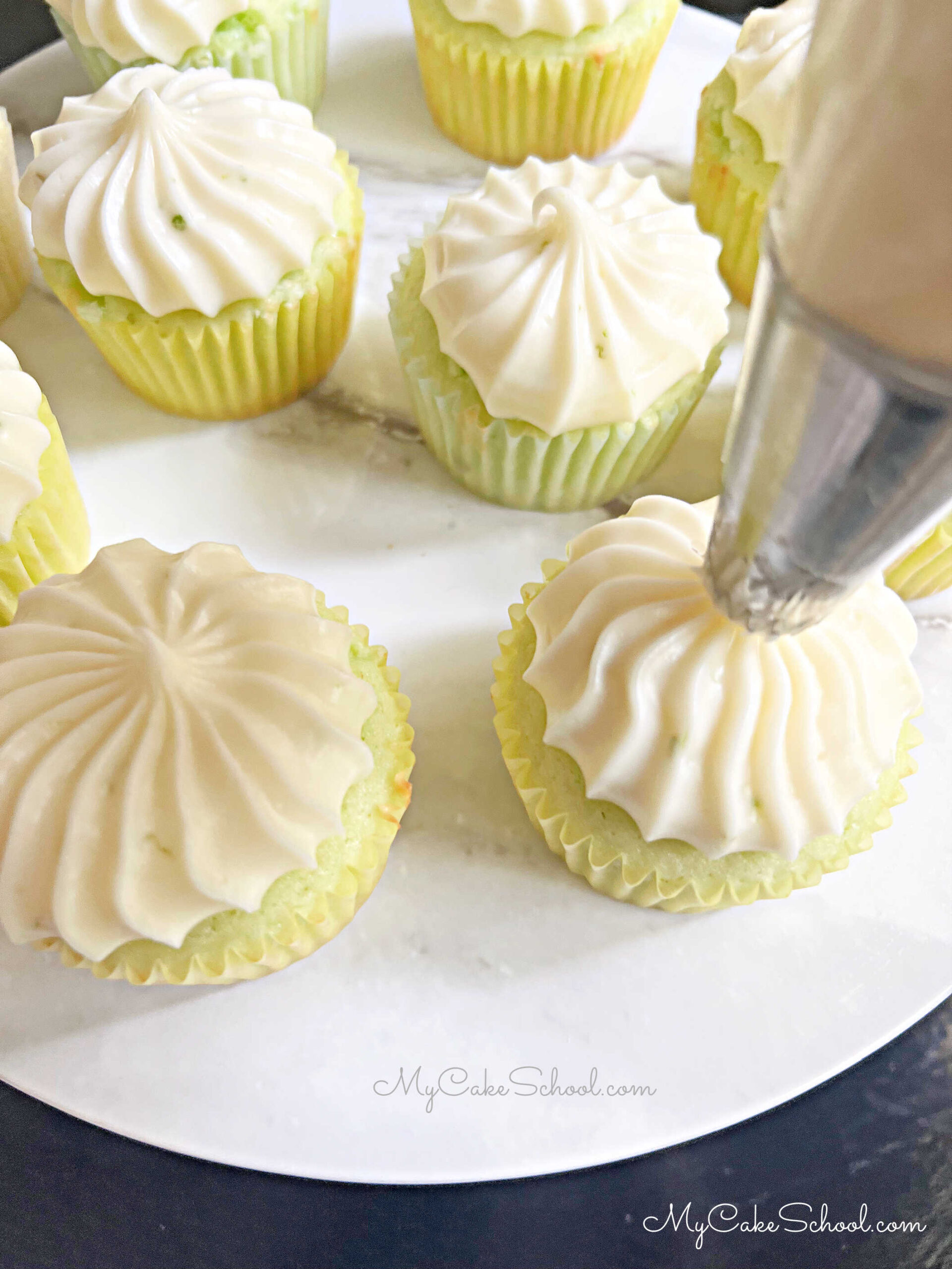 Piping tequila cream cheese frosting onto the margarita cupcakes.