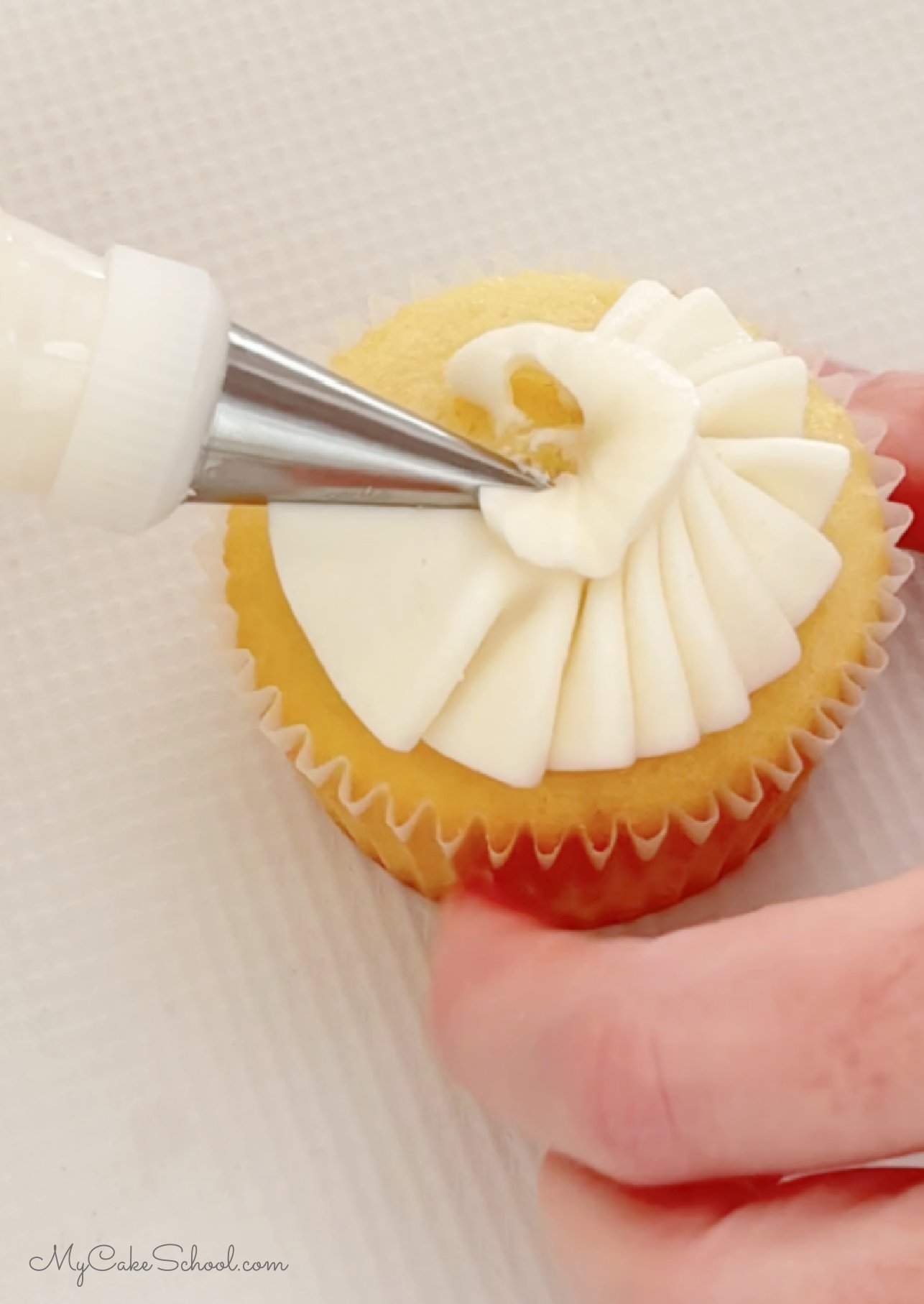 Piping ruffled buttercream onto the top of a vanilla cupcake using a tip 070