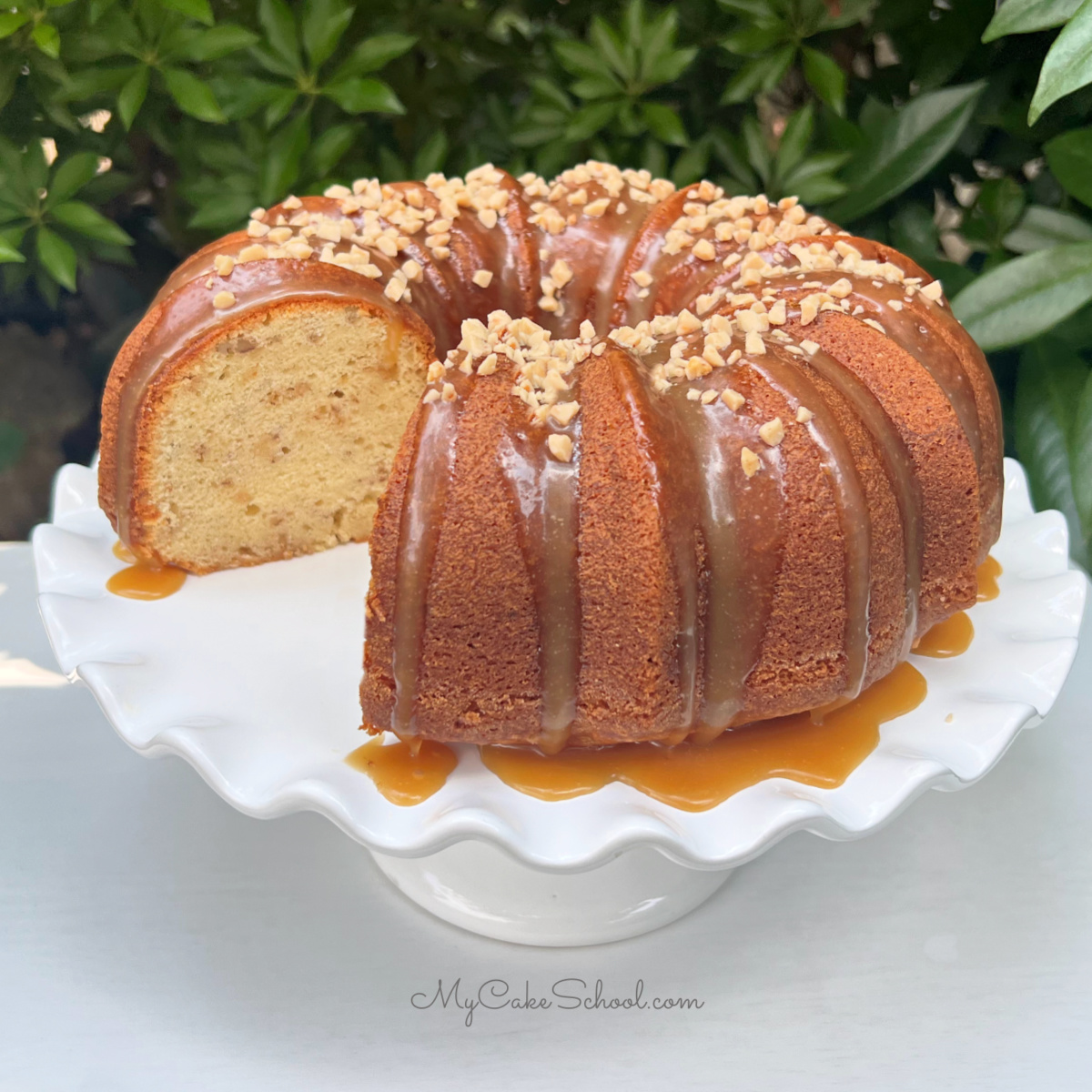 Sliced Toffee Pecan Bundt Cake with caramel glaze on a white pedestal. Top is sprinkled with toffee bits.