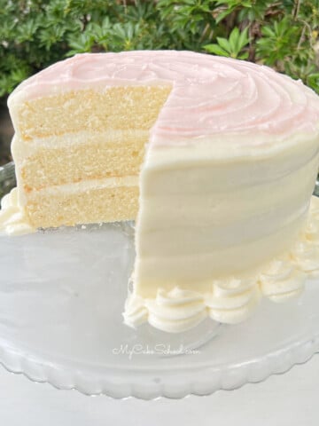 Sliced Homemade White Cake on a White Pedestal, topped with pink buttercream.