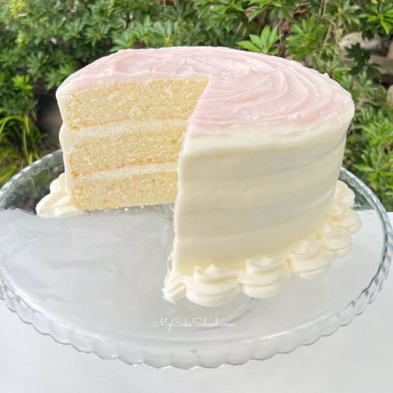 Sliced Homemade White Cake on a White Pedestal, topped with pink buttercream.