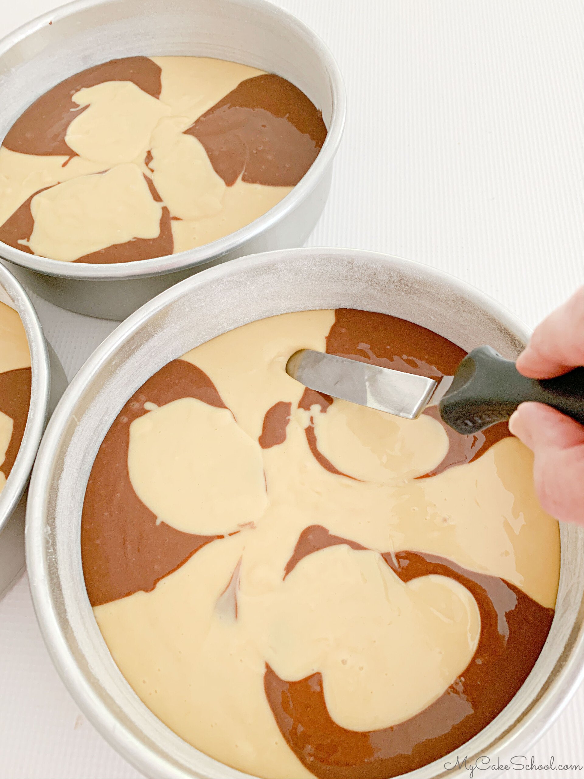 Marbling the yellow and chocolate cake batter in the three 8 inch cake pans, using a small offset spatula.