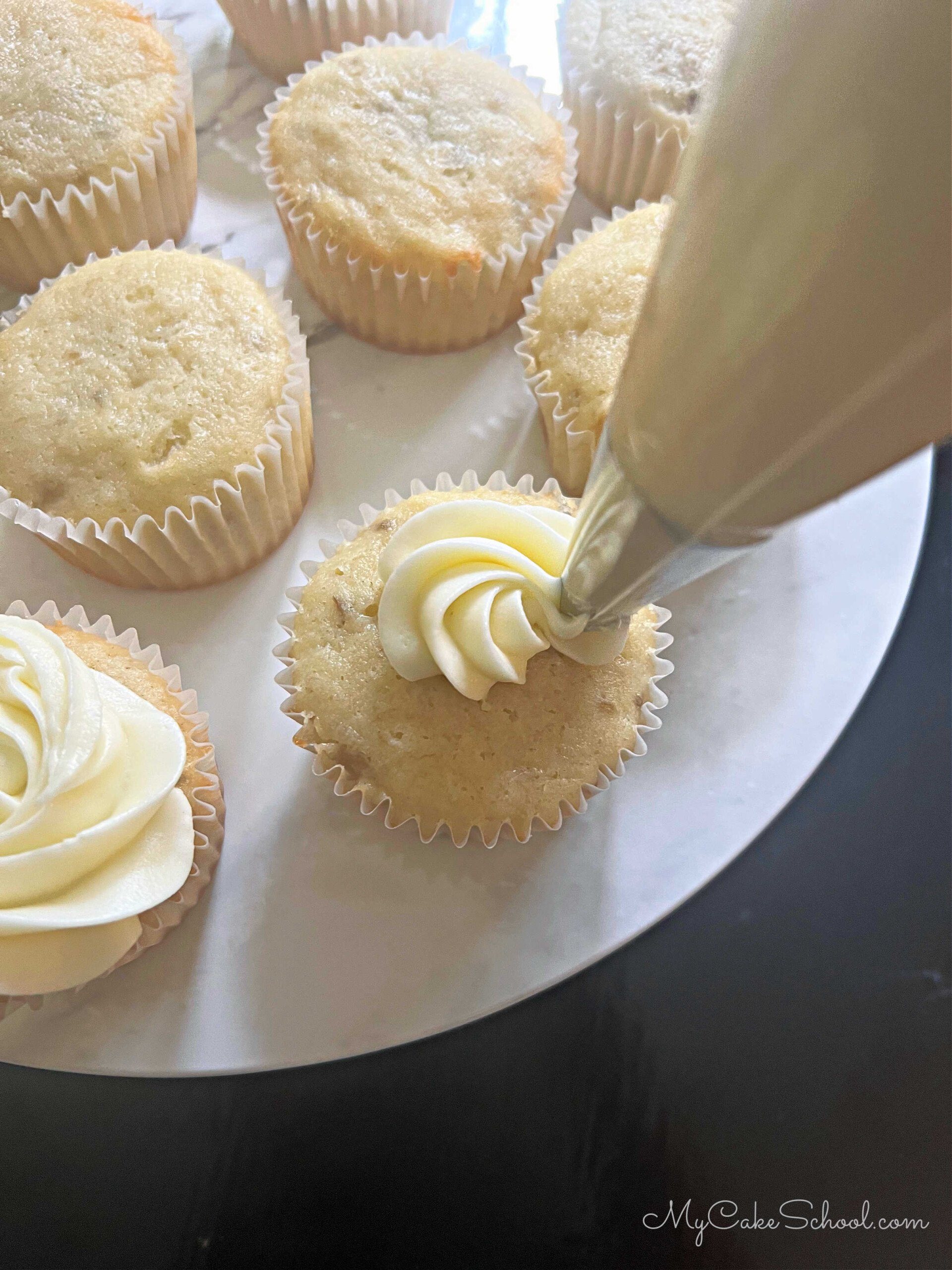 Frosting the banana cupcakes with cream cheese frosting.