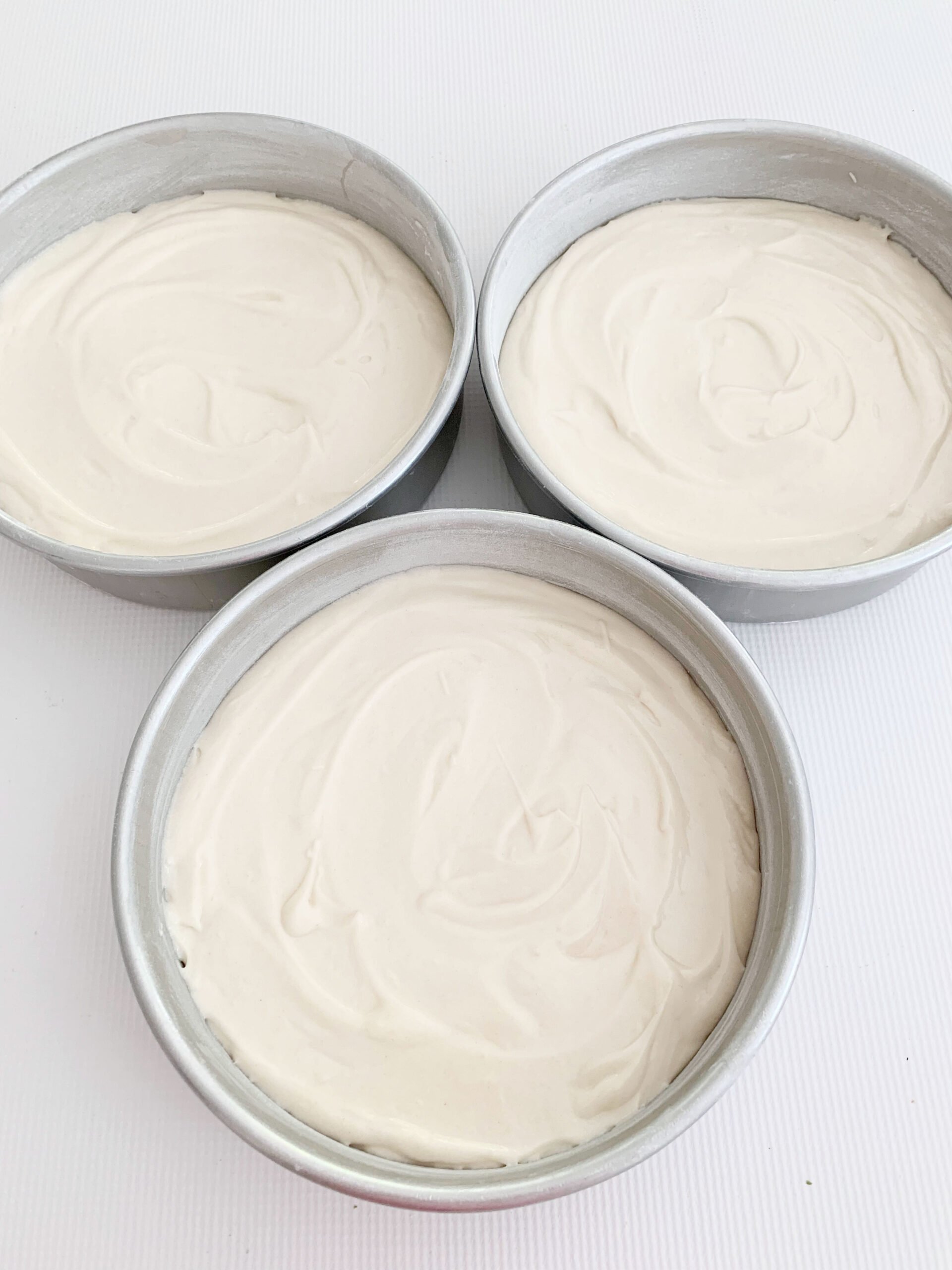 Three round cake pans of homemade white cake batter.