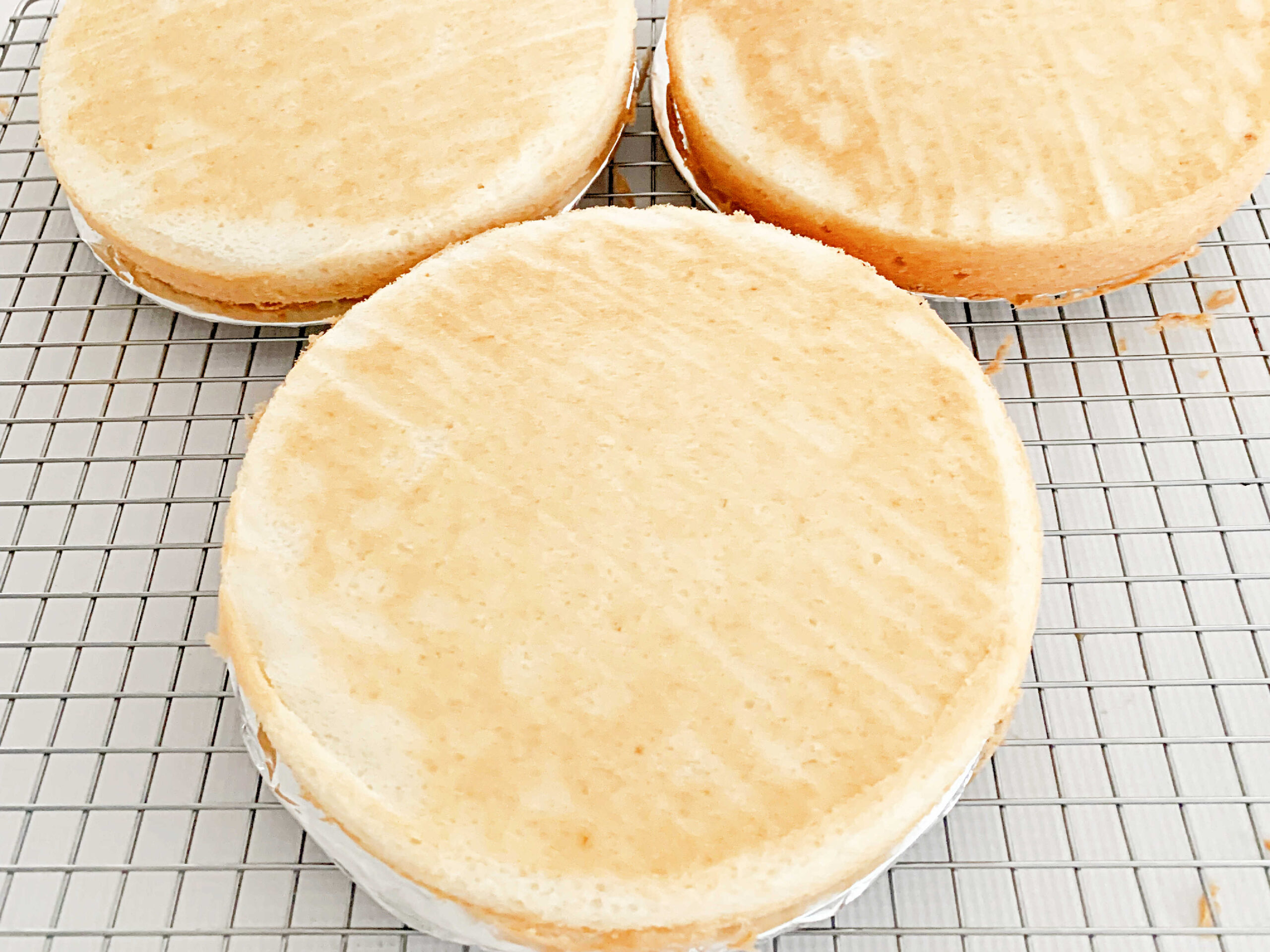 Three homemade white cake layers, turned out onto cake boards.