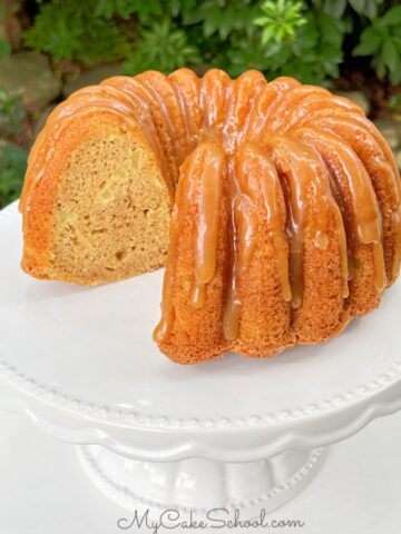 Sliced Apple Bundt Cake with caramel glaze on white pedestal.