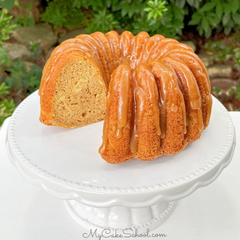 Sliced Apple Bundt Cake with caramel glaze on white pedestal.
