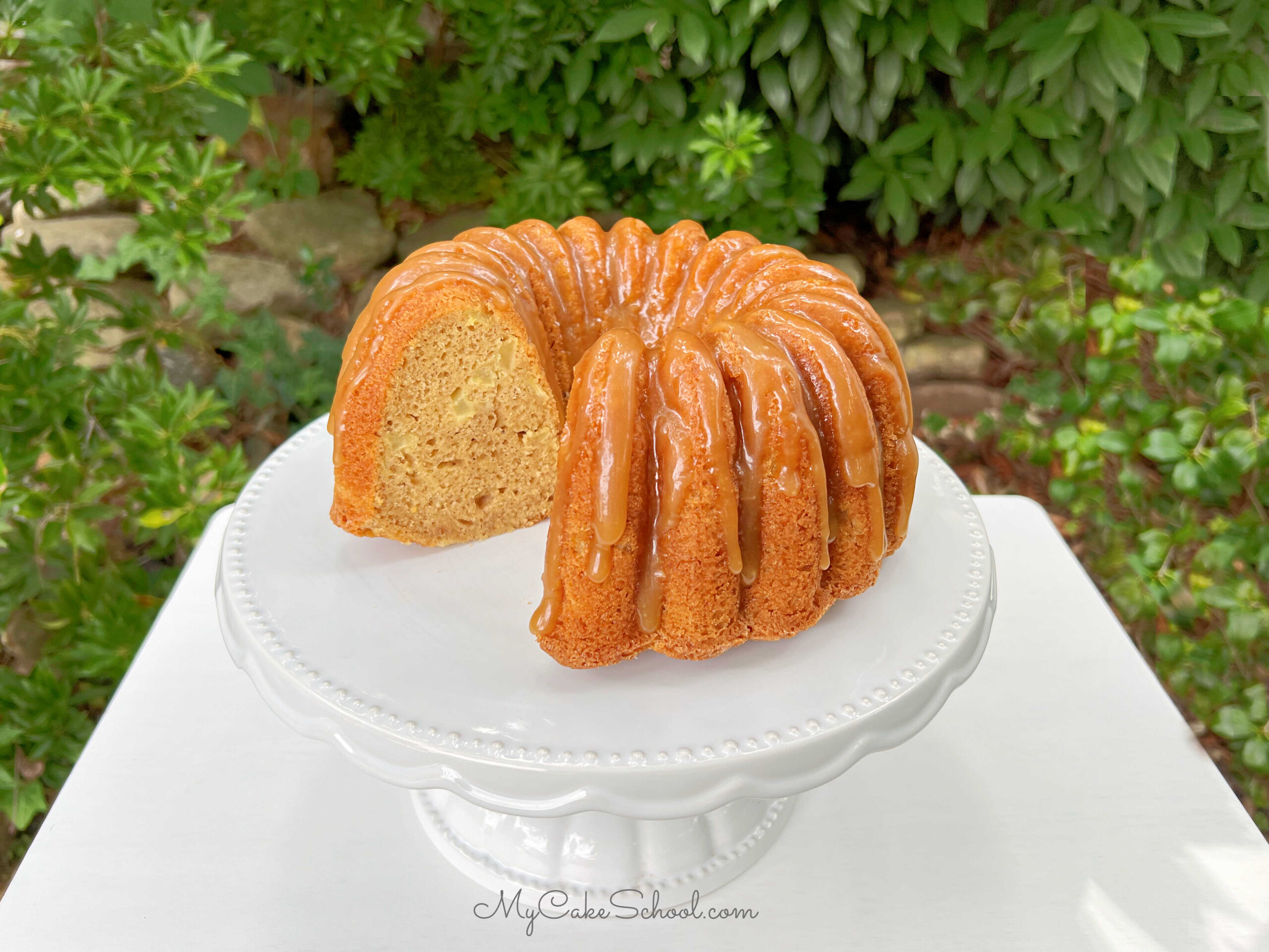 Apple Bundt Cake, sliced, with caramel glaze on white cake pedestal.