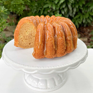 Sliced Apple Bundt Cake topped with caramel glaze, on a white cake pedestal.