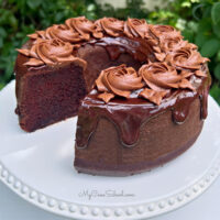 Sliced Chocolate Bundt Cake on a white cake pedestal, topped with chocolate glaze and chocolate buttercream rosettes.