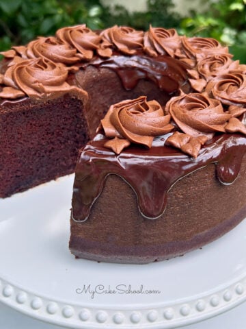 Sliced Chocolate Bundt Cake on a white cake pedestal, topped with chocolate glaze and chocolate buttercream rosettes.