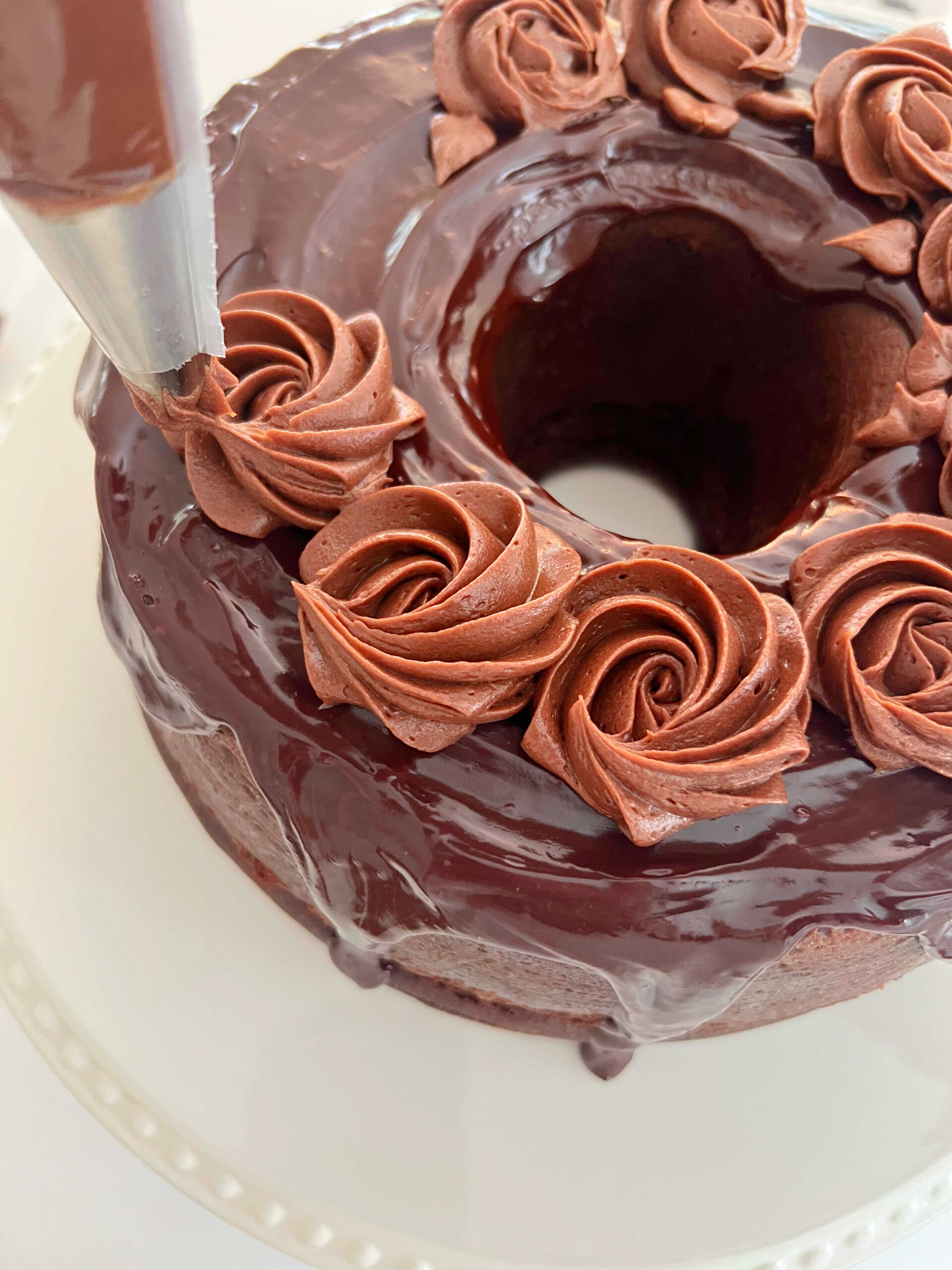 Piping Chocolate Buttercream Rosettes on top of the chocolate glazed bundt cake.
