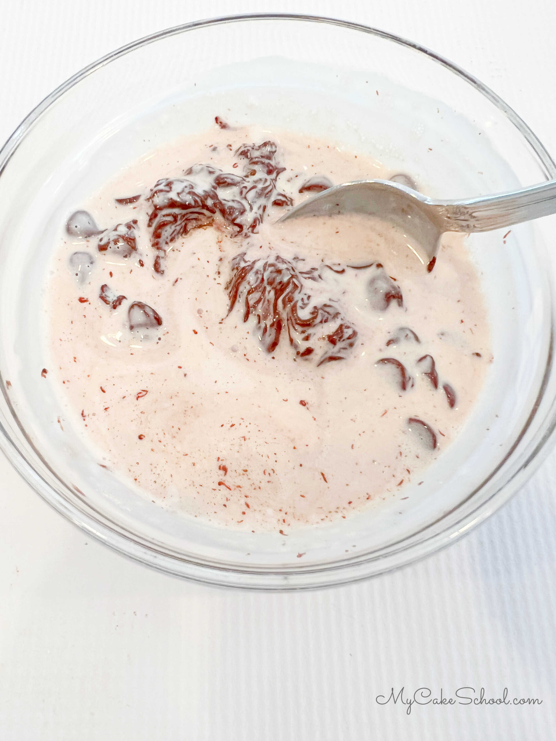 Stirring heated chocolate chips and heavy cream in a small glass bowl. 