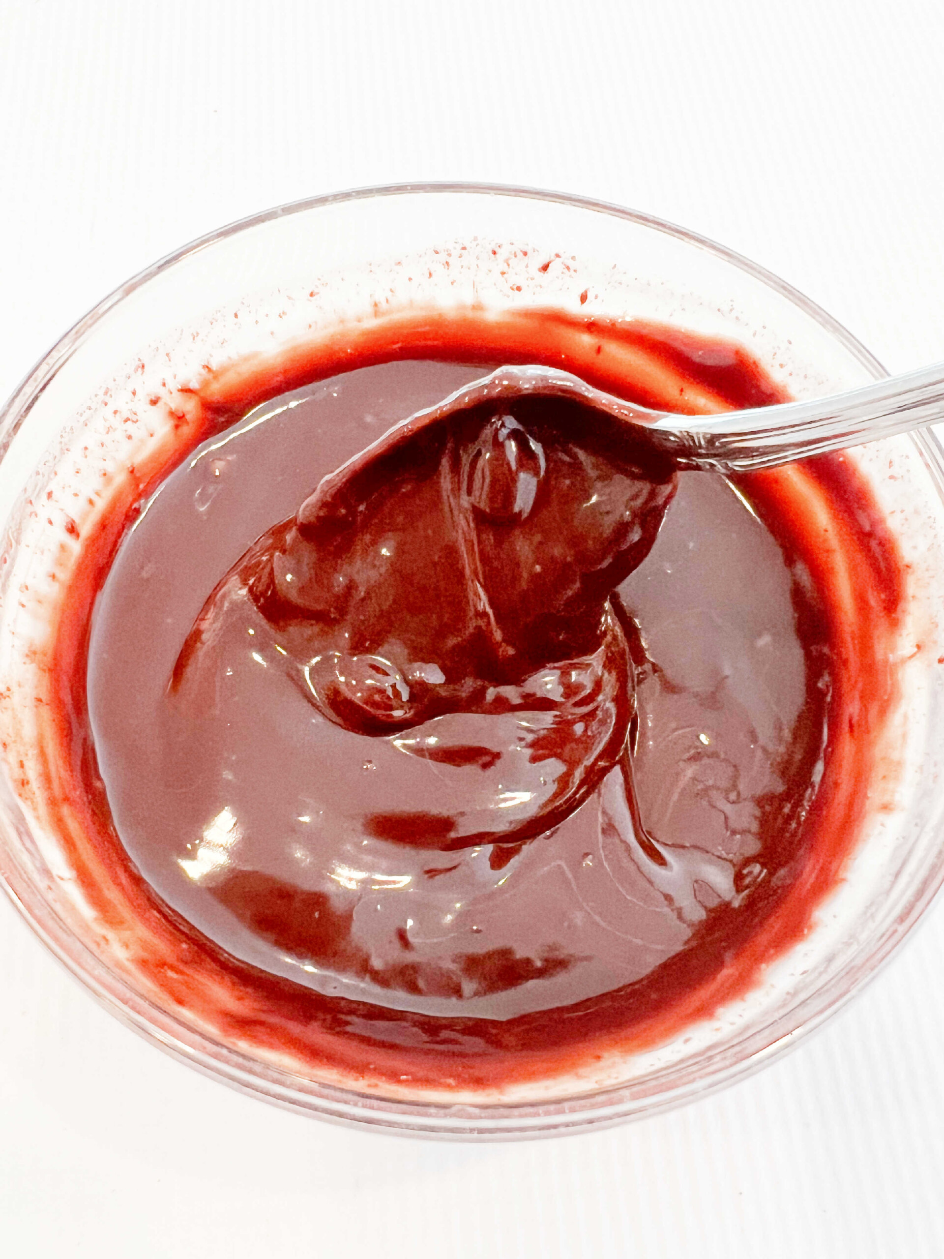 Stirring the completed chocolate glaze with a spoon in a small glass bowl.