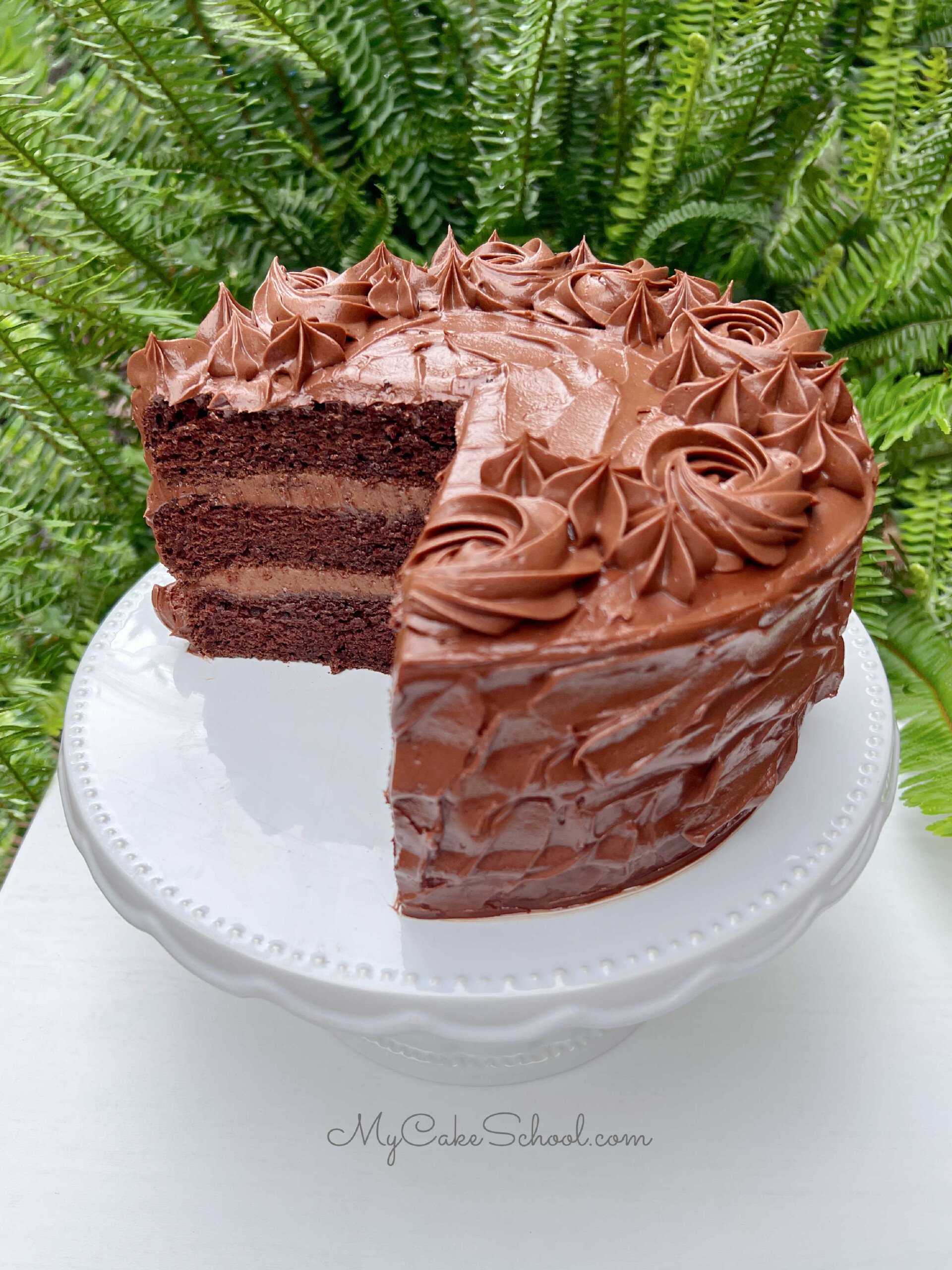 Chocolate Mousse Cake with chocolate frosting, sliced, on a white pedestal.