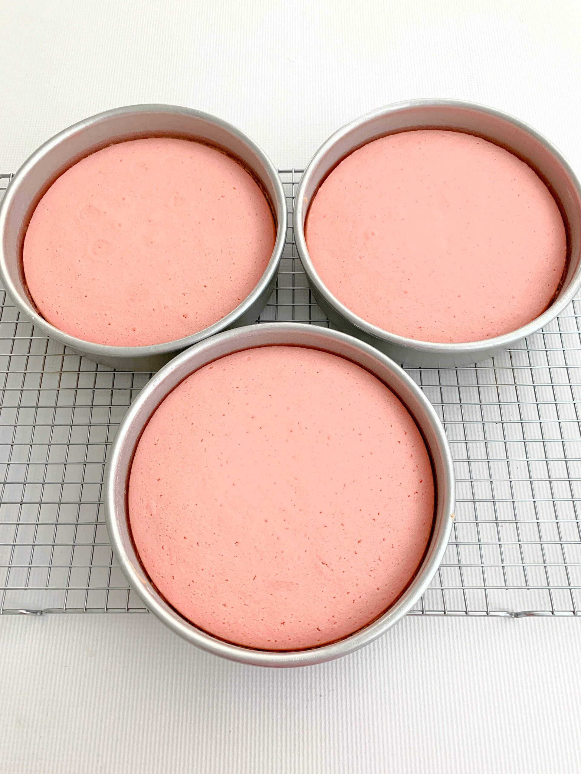 Freshly baked Pink Velvet Cake Layers, in pans on a cooling rack.