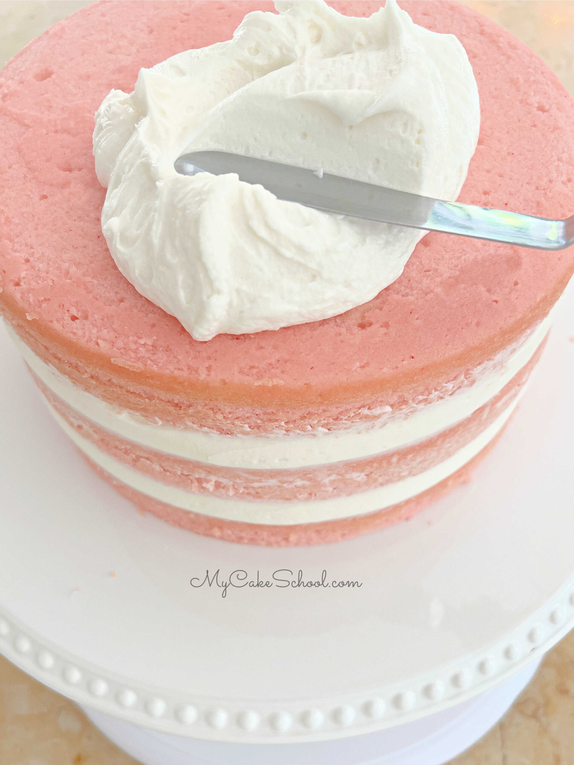 Frosting the three layer pink velvet cake with vanilla buttercream.