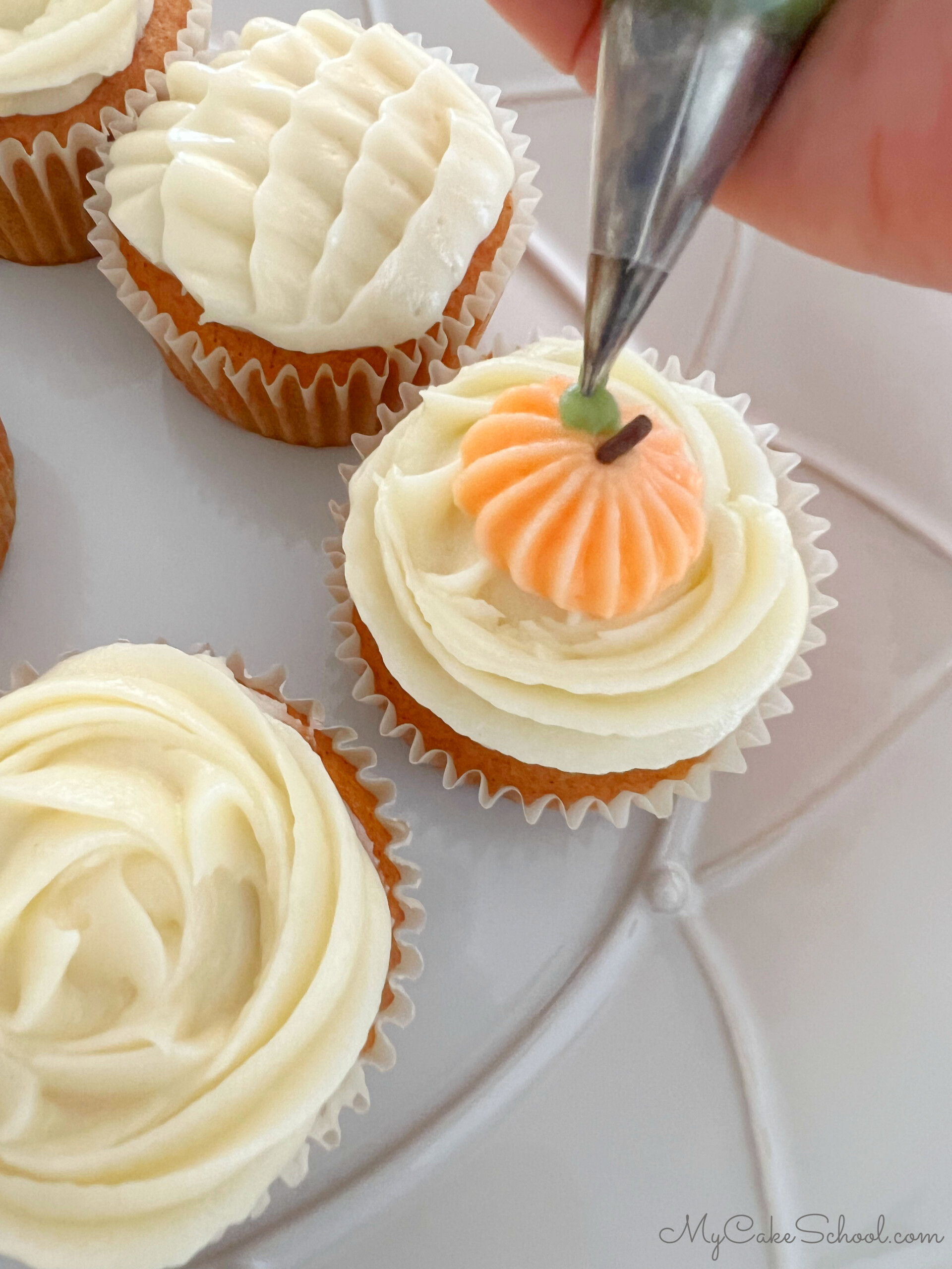 Piping decorative pumpkins and leaves on top of the frosted pumpkin cupcakes.