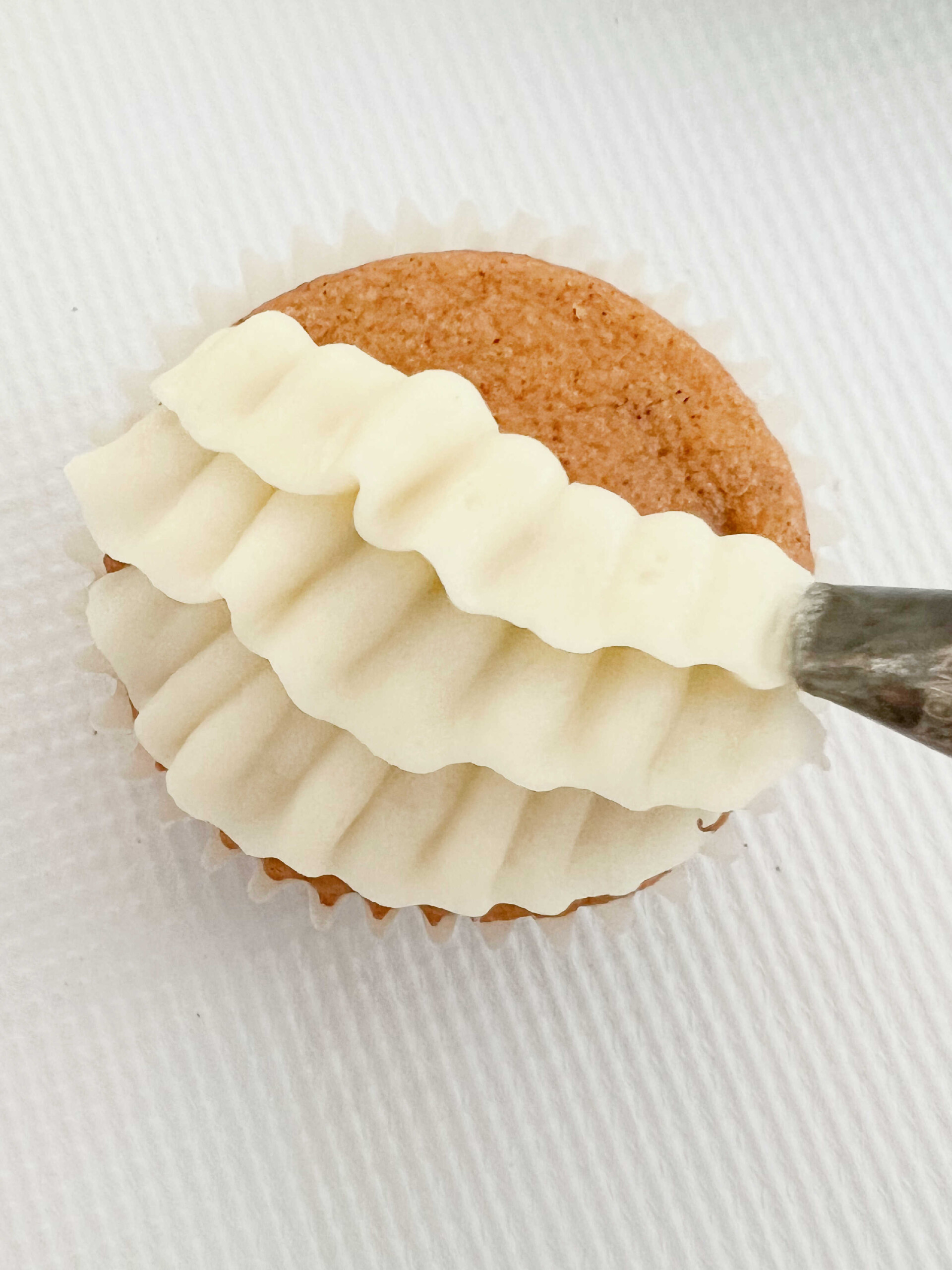 Piping rows of ruffled cream cheese frosting onto pumpkin cupcake with a 104 piping tip.