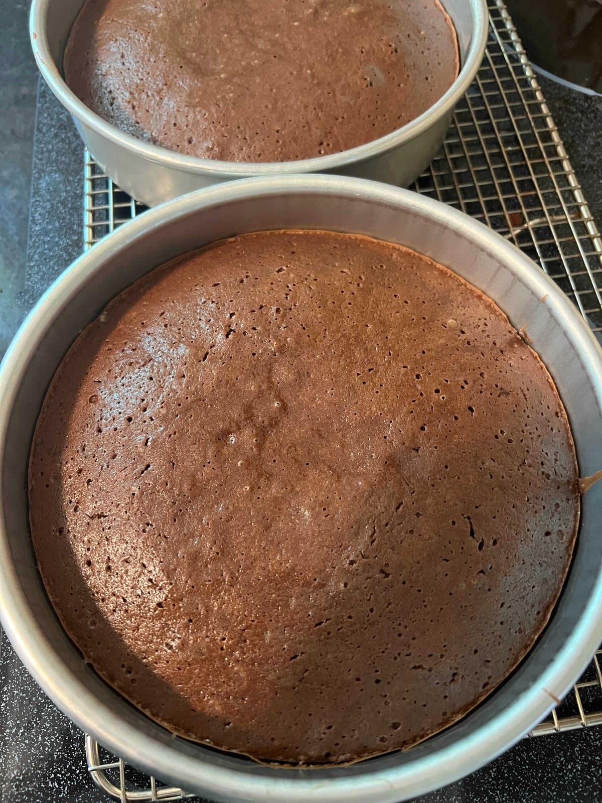 Two freshly baked brownie cake layers in pans on a wire rack.