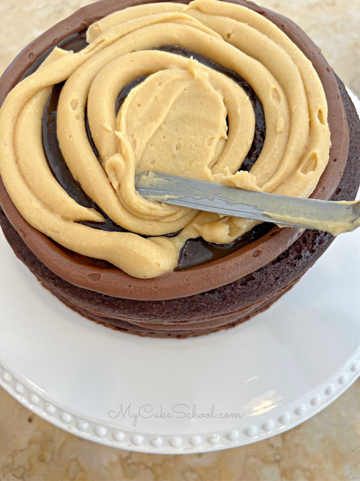 Spreading over the piped-on Caramel Cream Filling with an offset spatula.