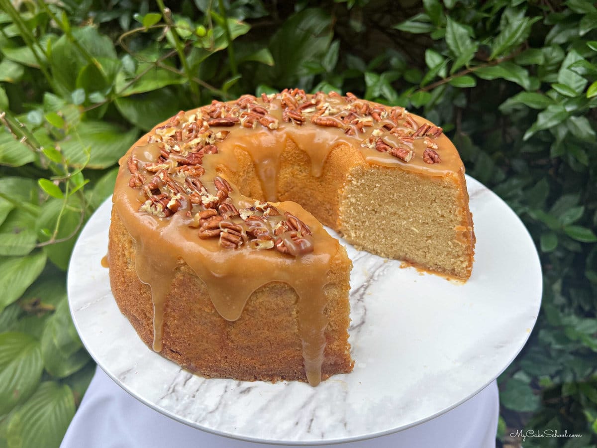 Sliced maple pound cake topped with caramel glaze and pecans, on pedestal.