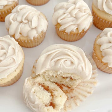 Platter of Snickerdoodle Cupcakes, with one of them sliced to reveal swirl of cinnamon.