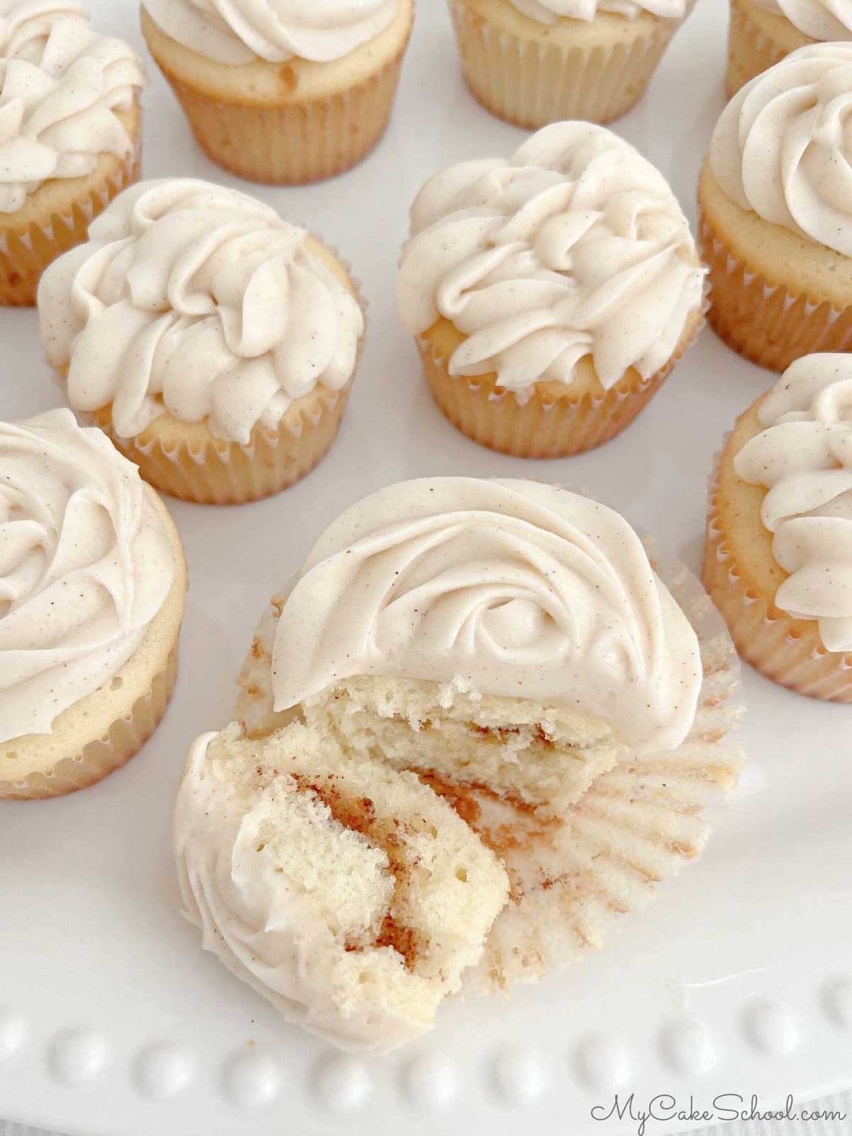 Platter of Snickerdoodle Cupcakes, with one of them sliced to reveal swirl of cinnamon.