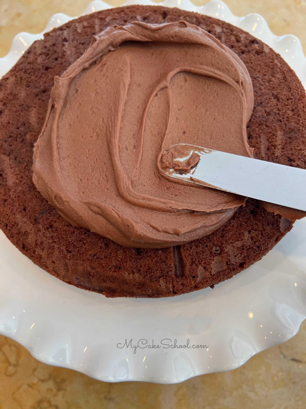 Frosting a layer of chocolate buttercream onto chocolate cake layer.