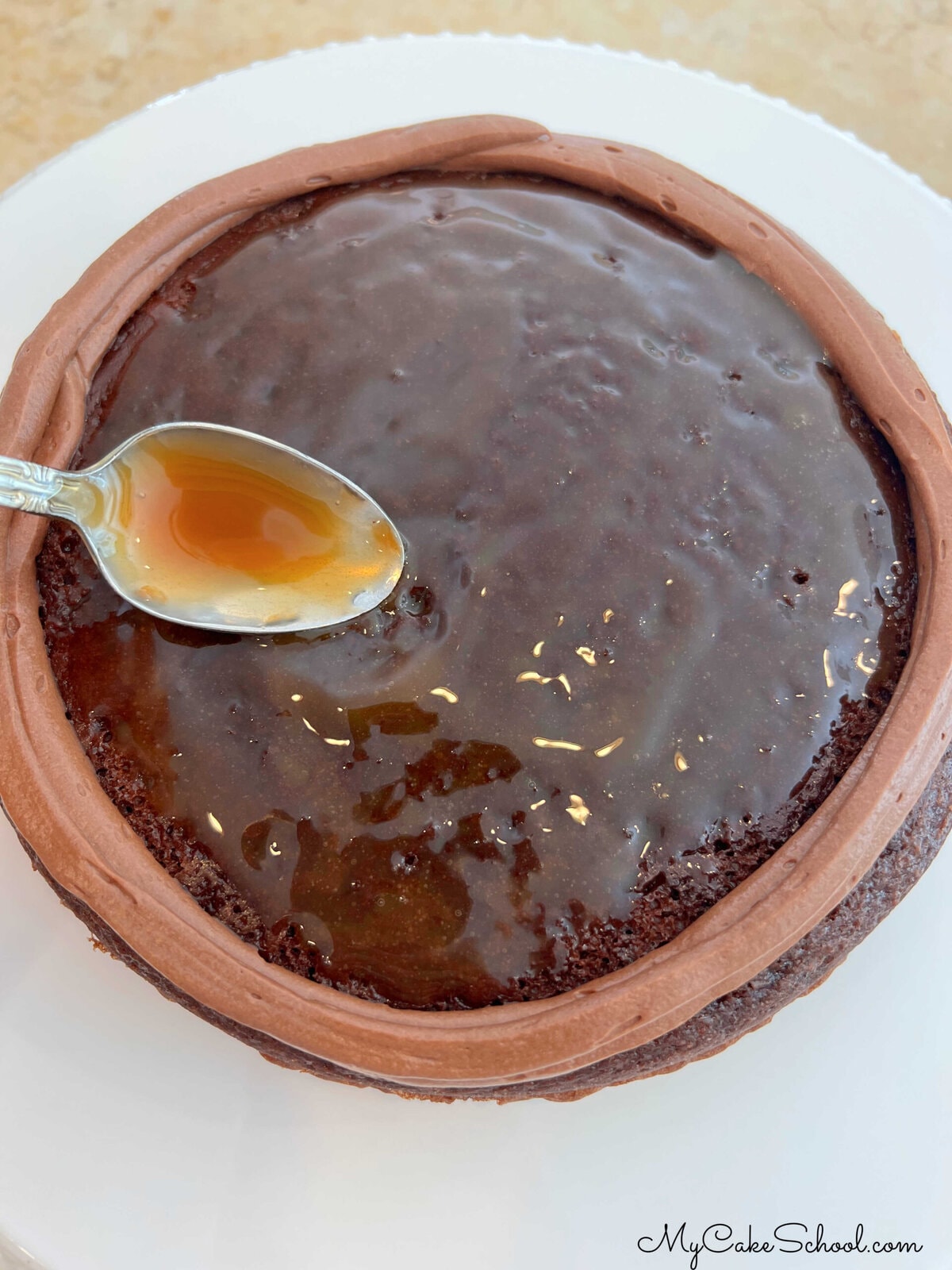 Spreading a thin glaze of caramel sauce over the chocolate cake layer. (Layer has chocolate buttercream dam.)
