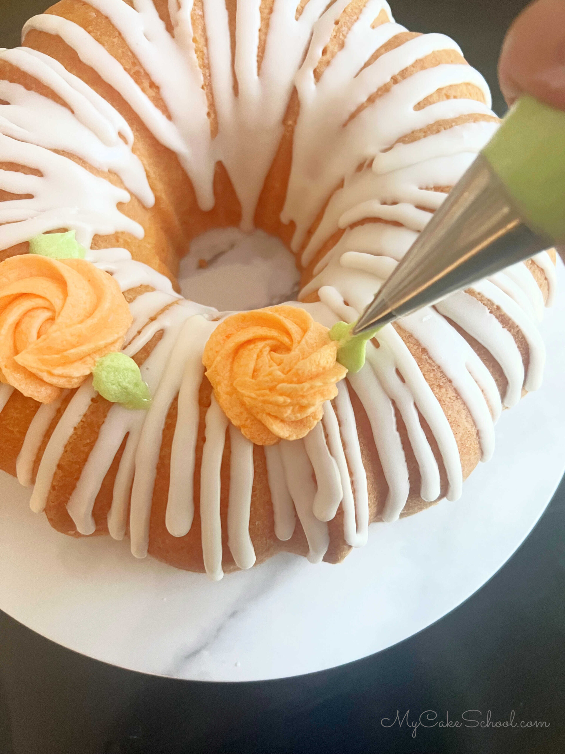 Piping rosettes and leaves onto glazed orange bundt cake.