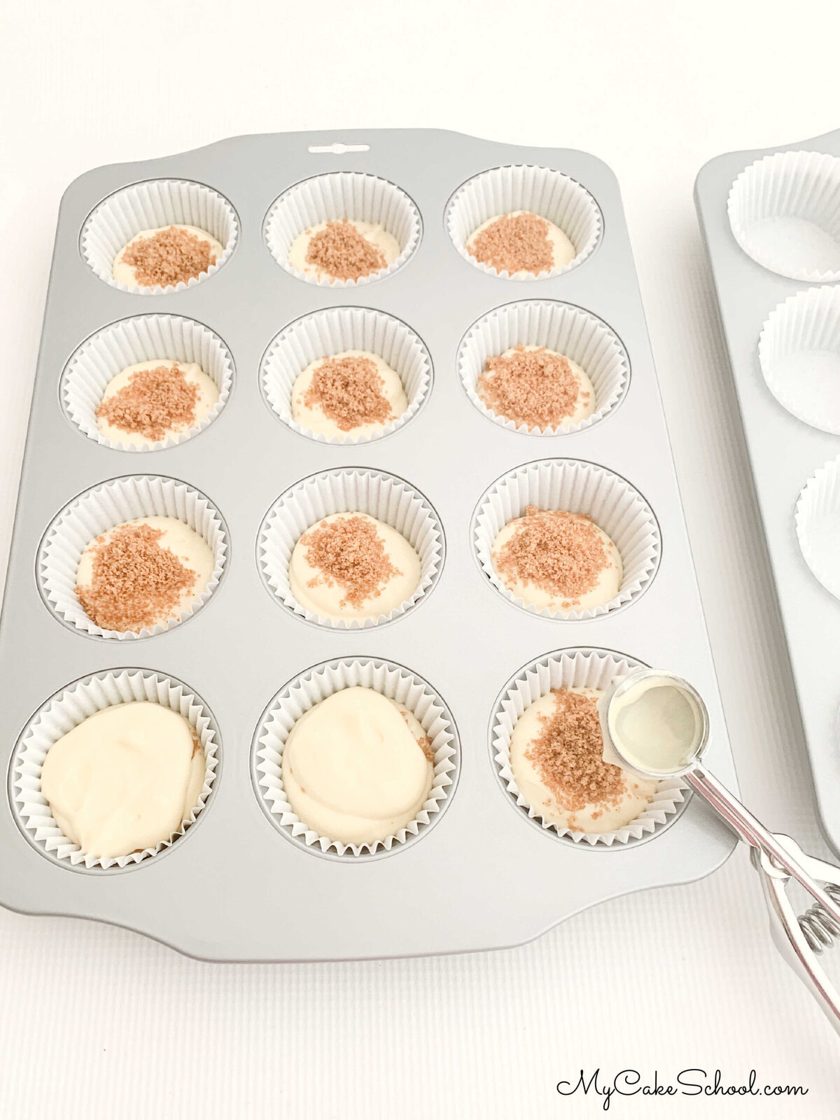 Filling cupcake liners with vanilla cupcake batter and a sprinkling of brown sugar and cinnamon.