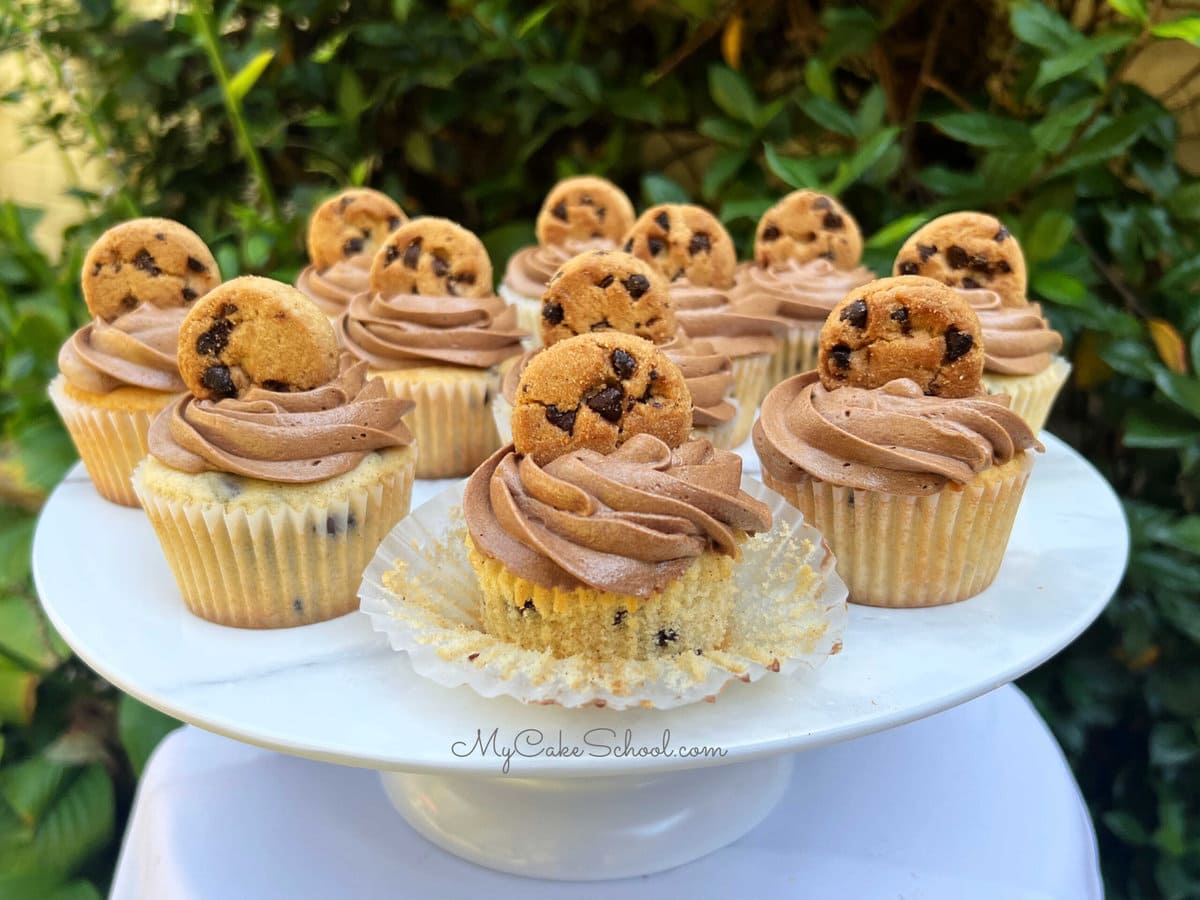 Chocolate Chip Cupcakes on a cake pedestal, topped with chocolate frosting and mini cookies.