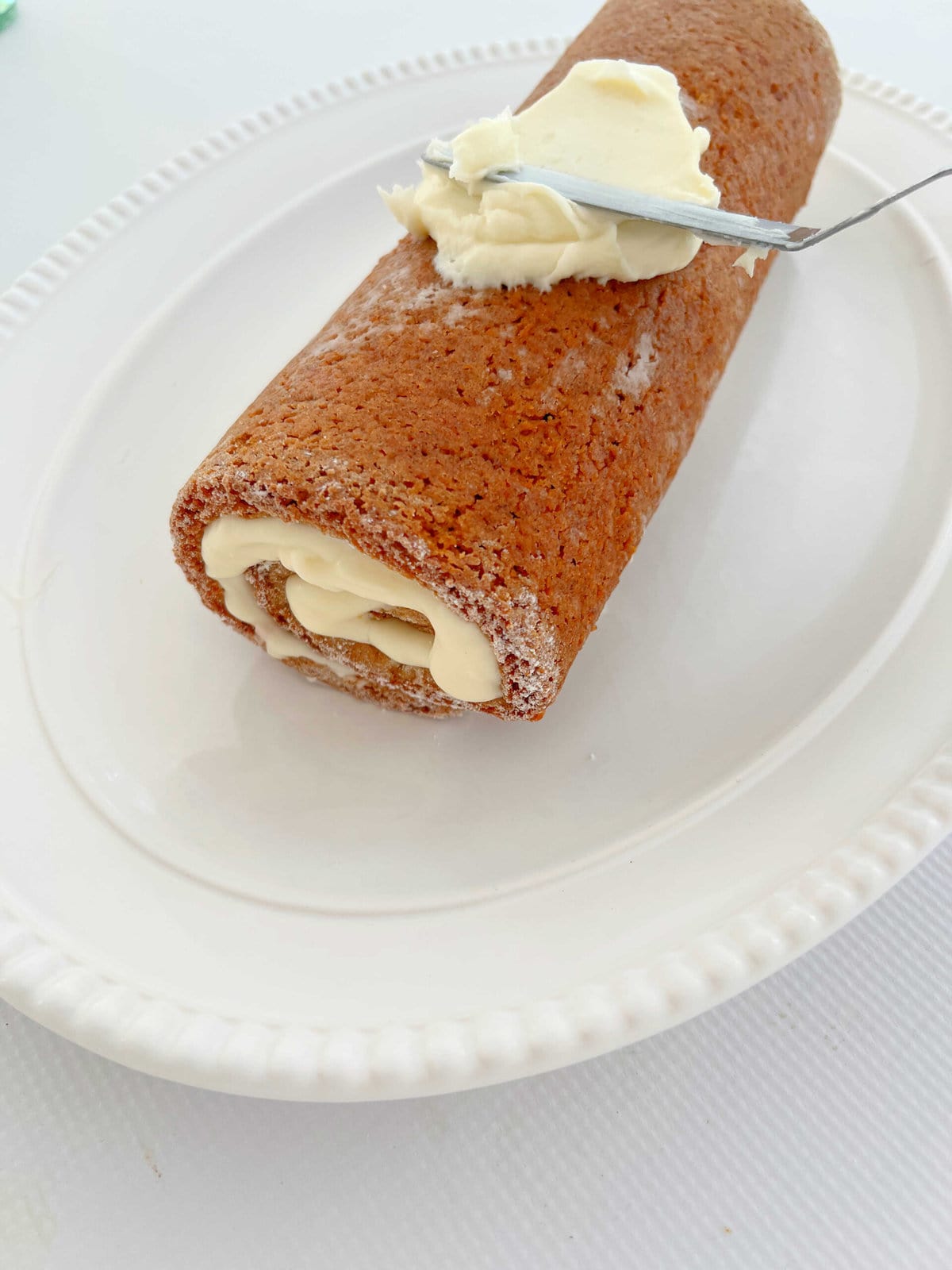 Frosting the Pumpkin Roll with Cream Cheese Frosting.