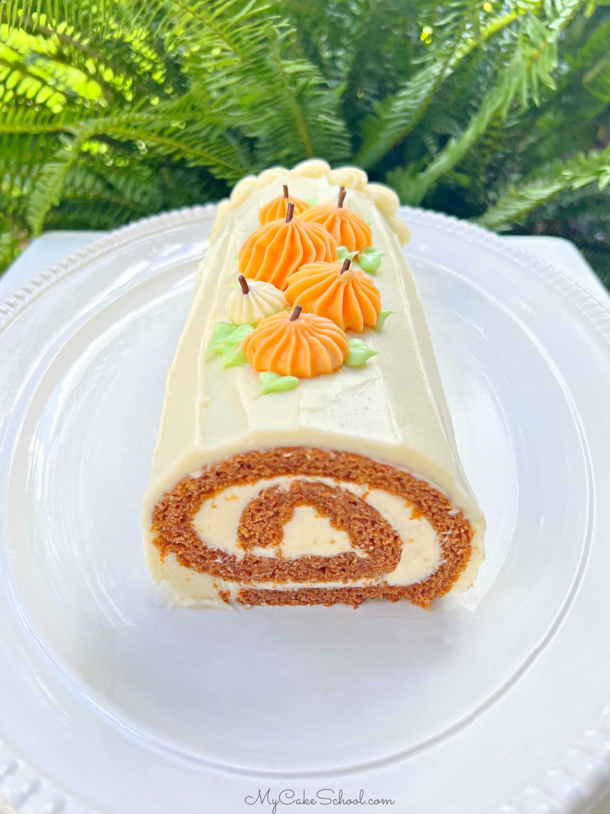 Pumpkin Roll on a platter, frosted with cream cheese frosting and topped with piped pumpkins.