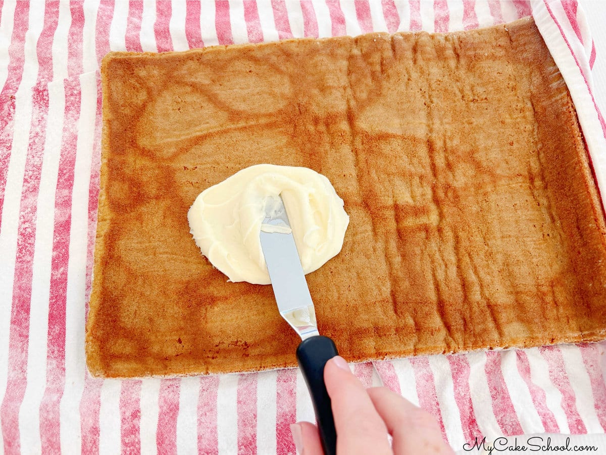 Spreading frosting onto the unrolled pumpkin cake layer.