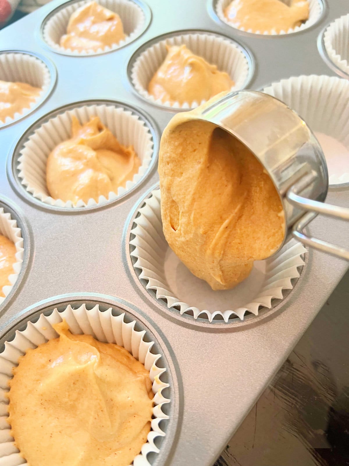 Filling the cupcake liners with sweet potato cake batter, using a ¼ measuring cup.