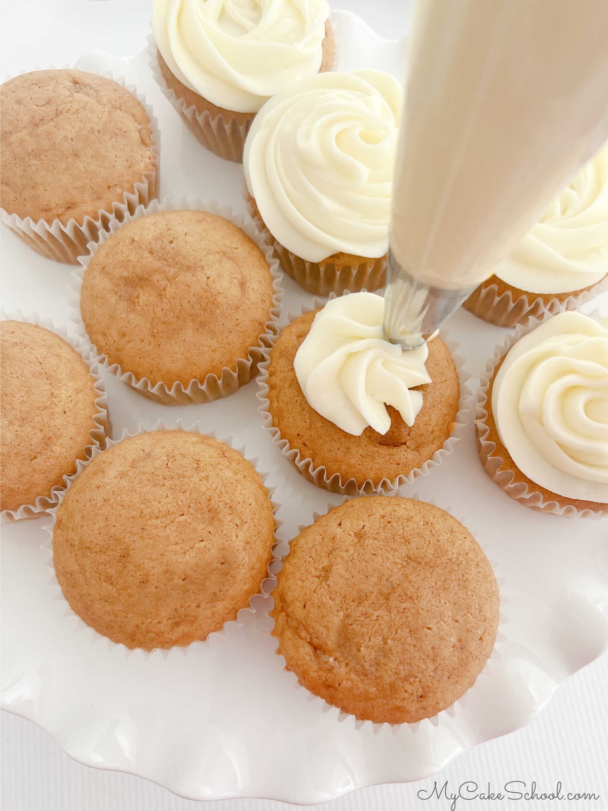 Piping swirls of cream cheese frosting onto the sweet potato cupcakes.