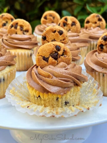 Chocolate Chip Cupcakes on a cake pedestal, topped with chocolate frosting and a mini cookie.