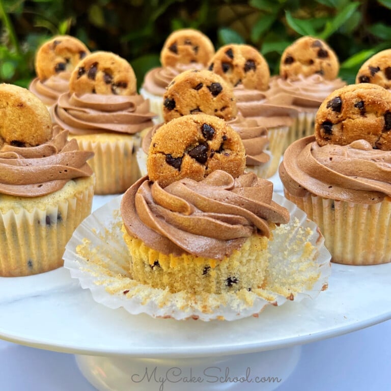 Chocolate Chip Cupcakes on a cake pedestal, topped with chocolate frosting and a mini cookie.